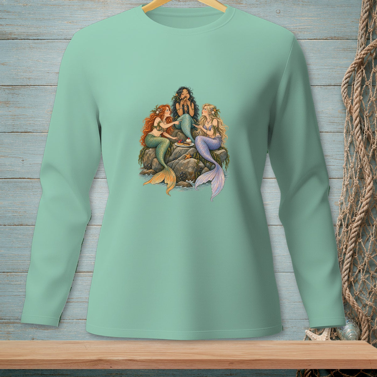 Three mermaids with tails gather on rocks to share cake.