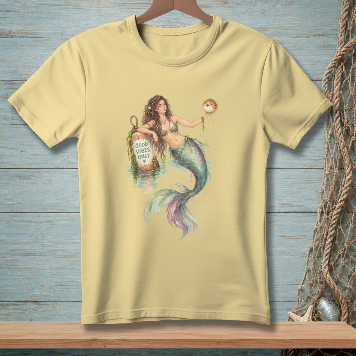 Mermaid with pufferfish and buoy reading "GOOD VIBES ONLY" on yellow t-shirt.
