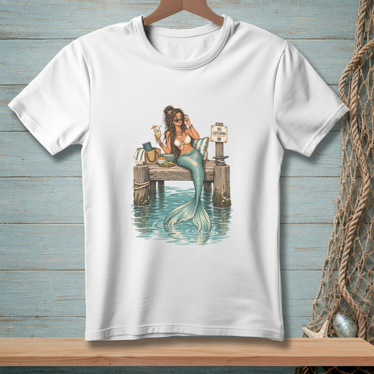 White t-shirt with illustration of a mermaid relaxing on a dock with a "No Loitering" sign.