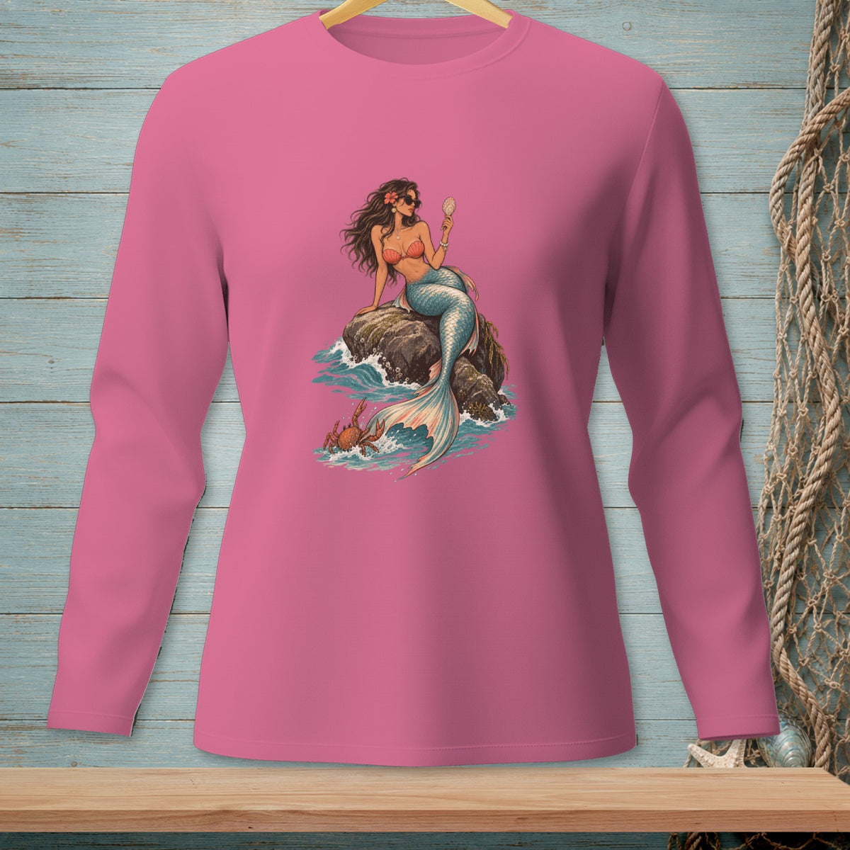 Pink long-sleeve shirt with mermaid and crab graphic on a rock in the ocean.