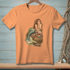 Peach t-shirt with a mermaid sitting on rocks surrounded by sea treasures.