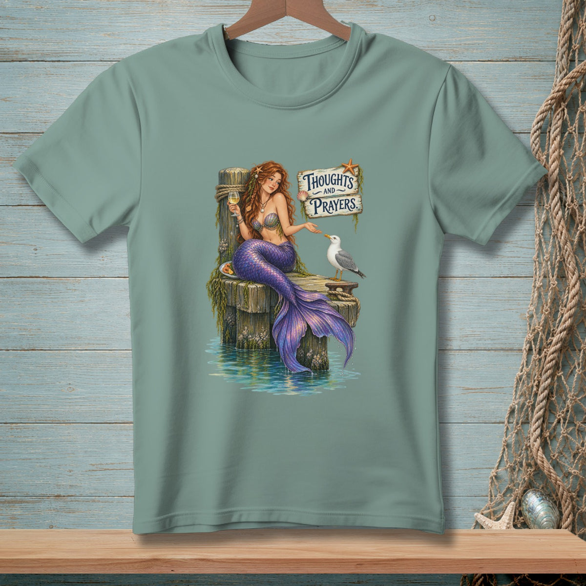 Mermaid with a glass of wine and a seagull on a pier with "Thoughts and Prayers" sign.