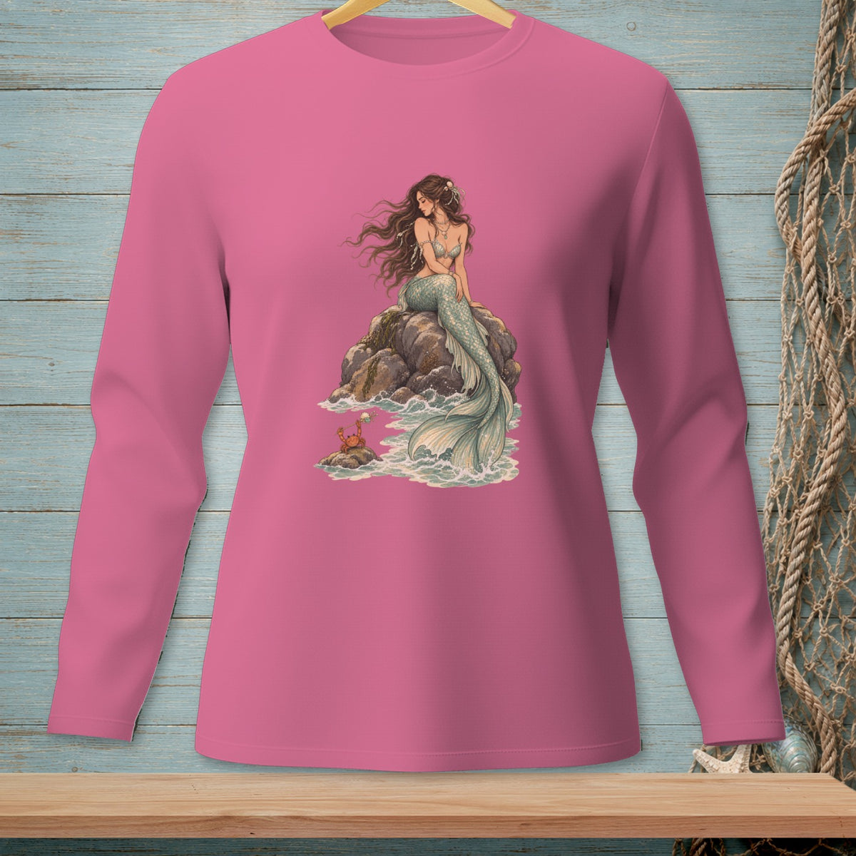 Pink long-sleeve shirt featuring a mermaid and crab on rocks by the ocean.