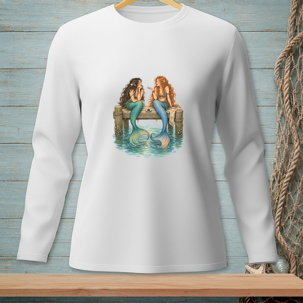 Two mermaids with colorful tails sitting on a wooden pier by the water.