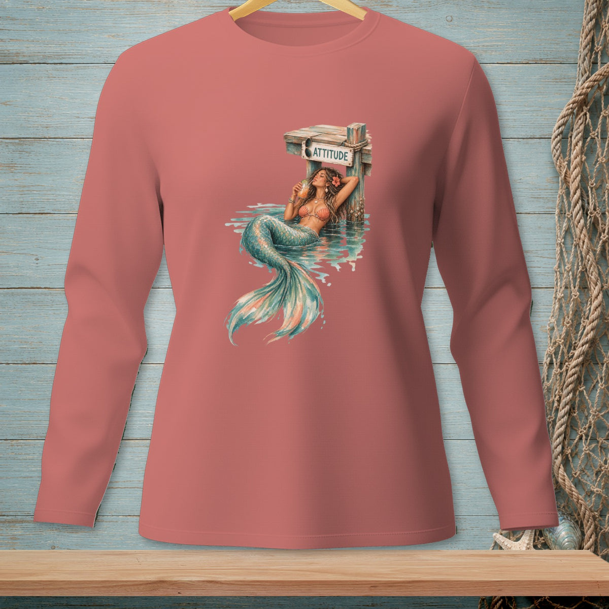 Mermaid with cocktail leans on sign reading ATTITUDE, on coral long sleeve shirt.