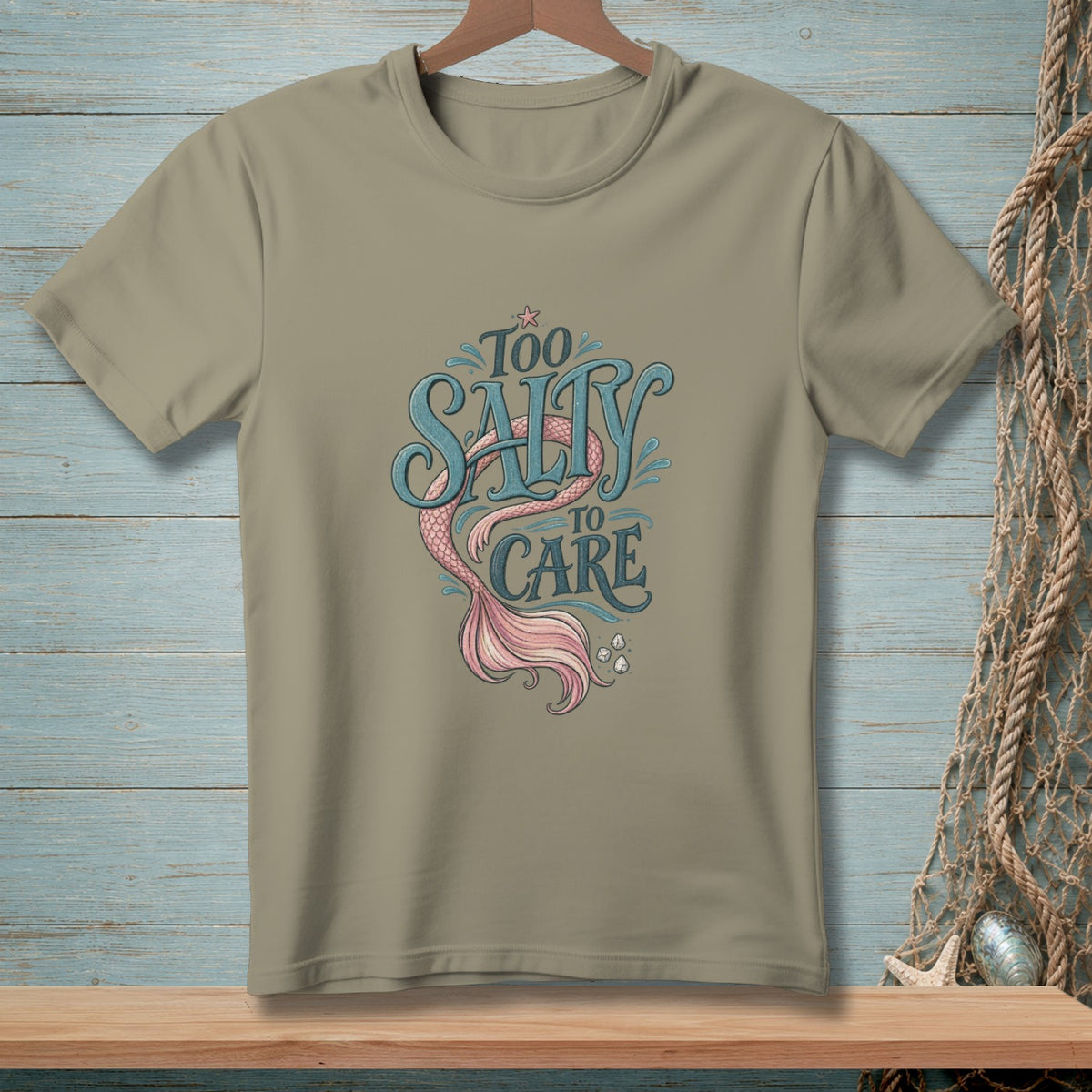 Tan t-shirt with "Too Salty To Care" text and a pink mermaid tail illustration.