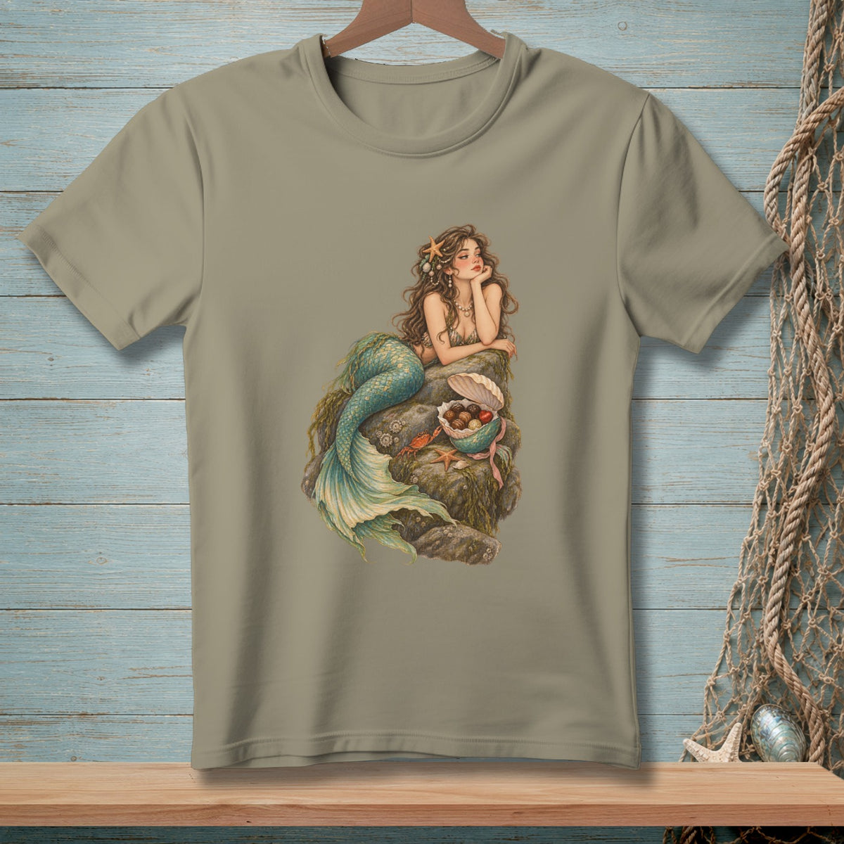 T-shirt with mermaid sitting on rocks holding seashells and chocolate candies.