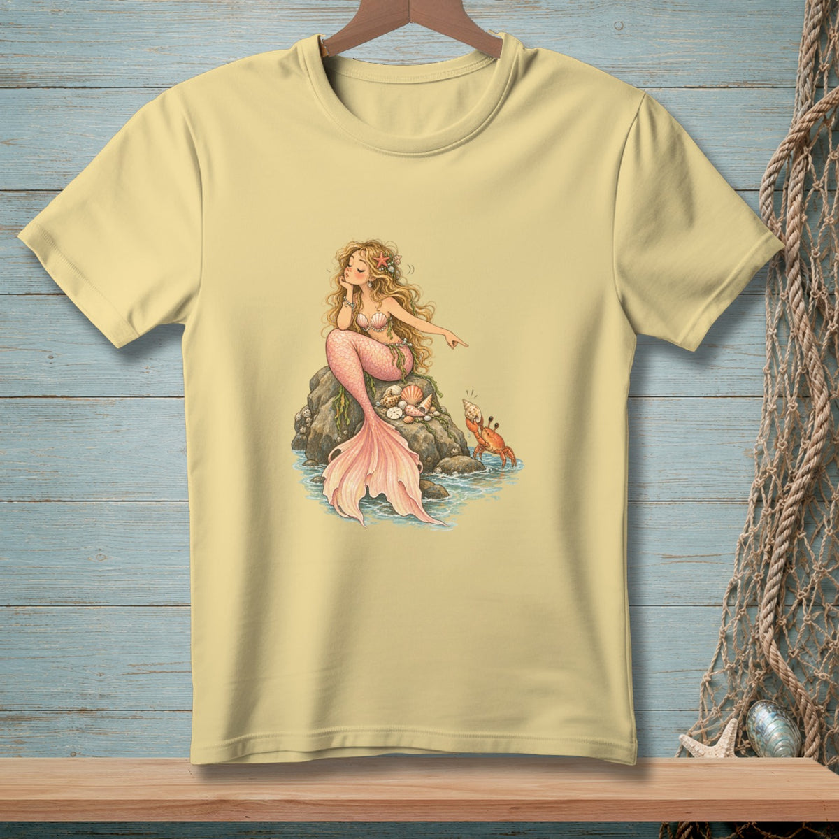 Yellow t-shirt with a drawing of a mermaid pointing at a crab on a rock.