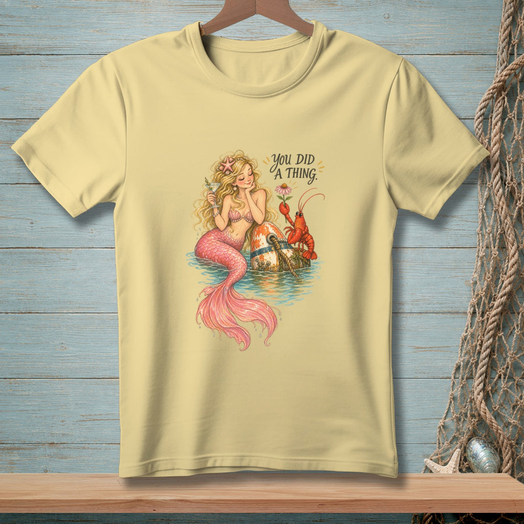 Mermaid with lobster and text "You DID A THING." on a light yellow t-shirt.