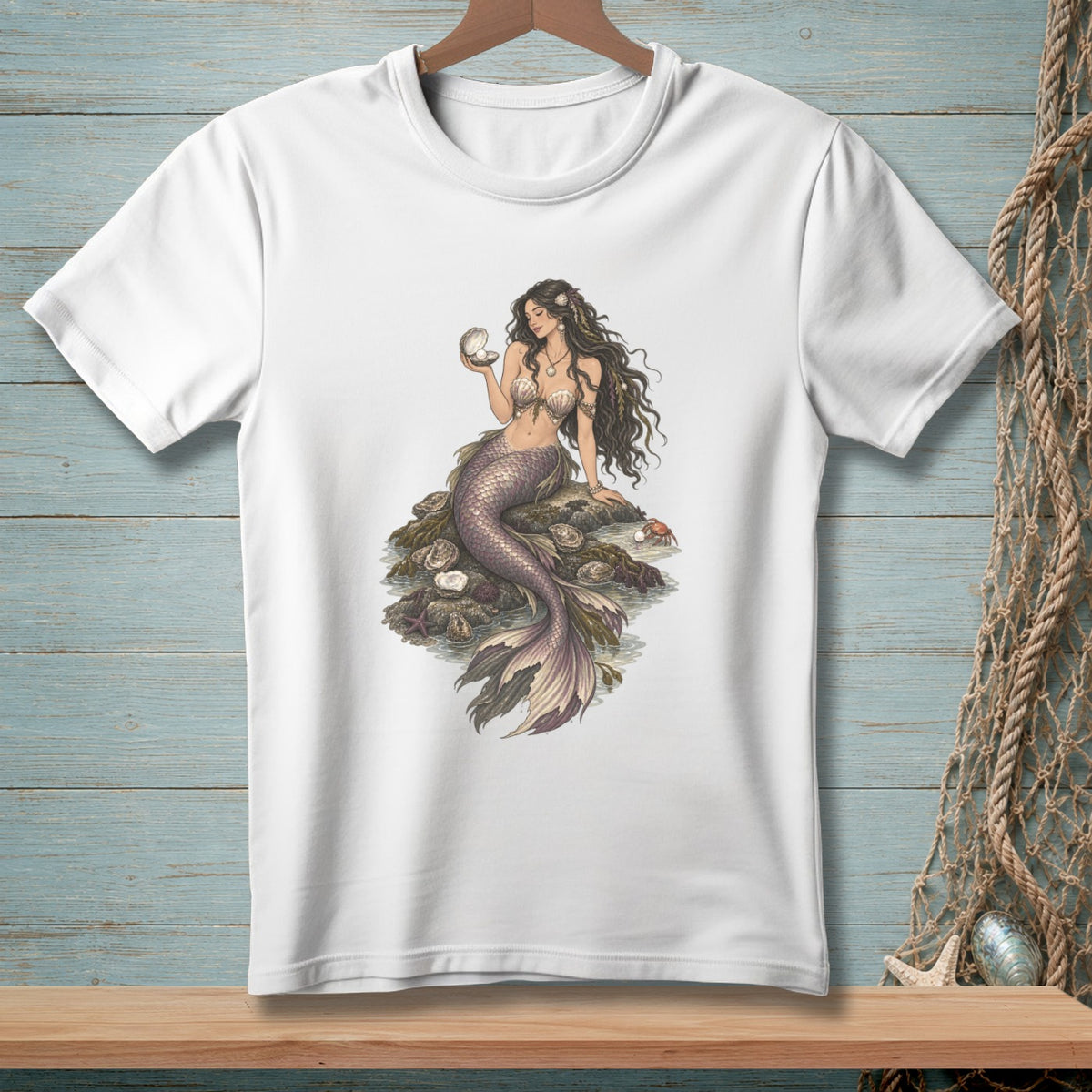 White t-shirt with illustration of a mermaid holding a pearl on a rock surrounded by shells.
