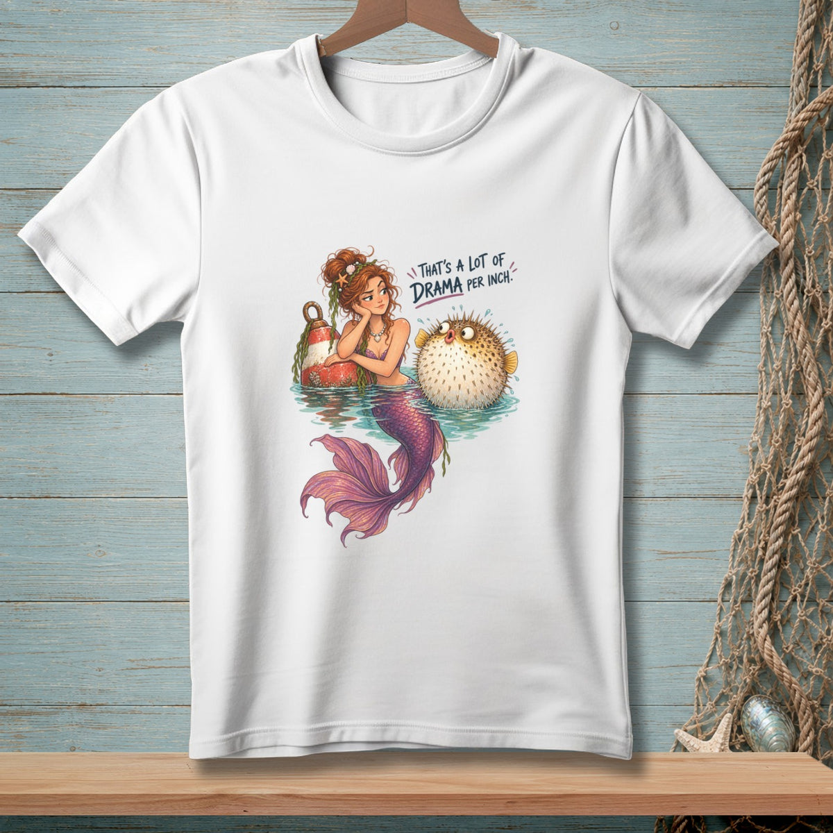 White t-shirt with a mermaid and pufferfish illustration that reads "That's a lot of drama per inch."