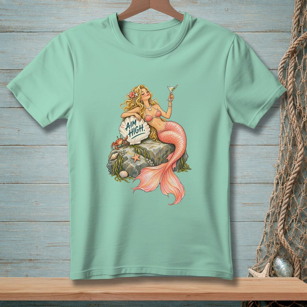 Mint t-shirt with mermaid artwork holding a martini, text "AIM HIGH" on a shell.