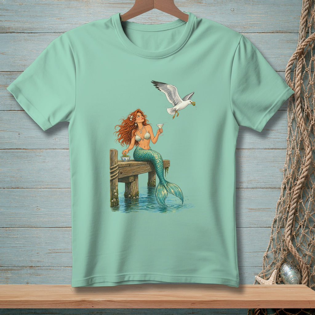 Mint t-shirt with mermaid on dock holding drink, seagull flies overhead.
