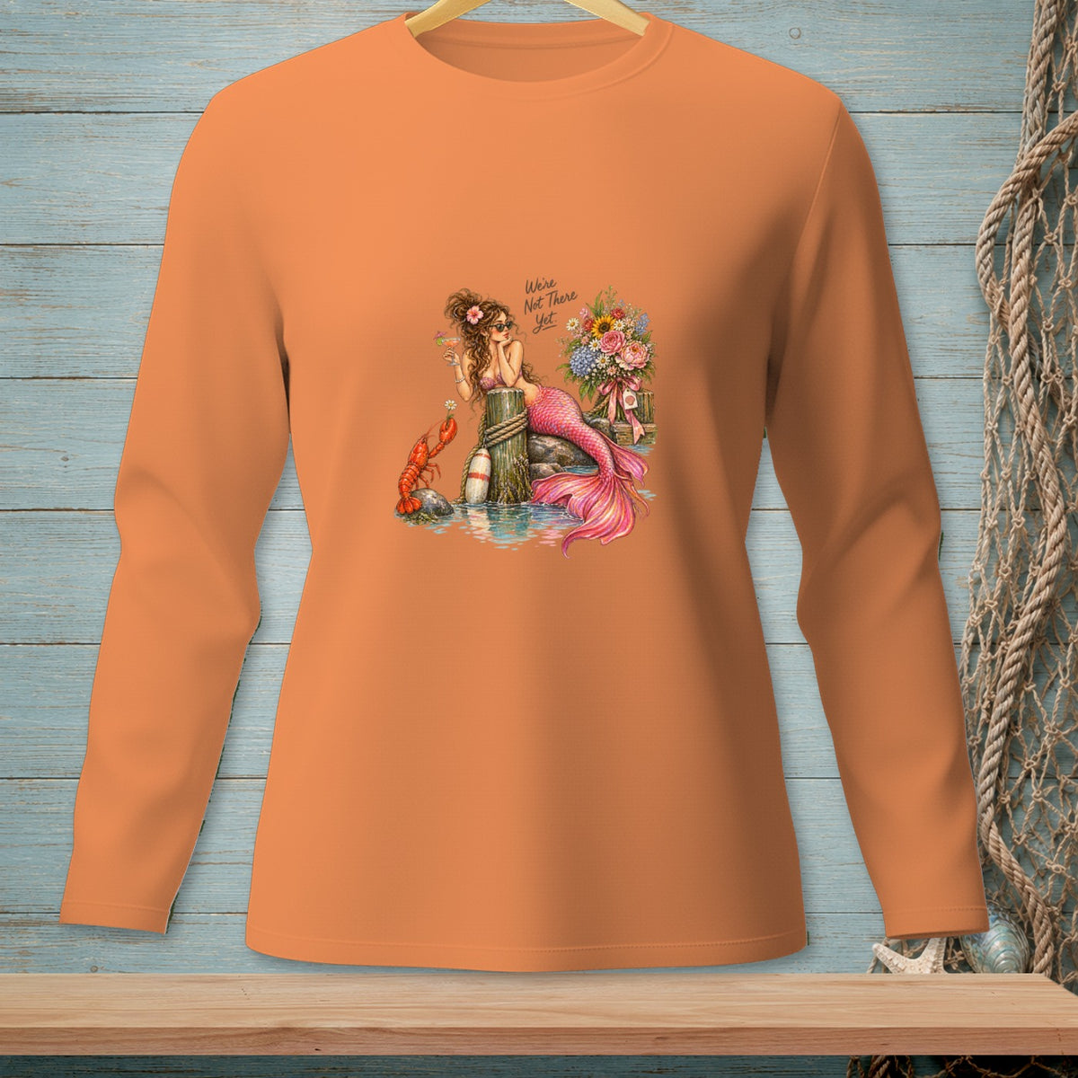 Orange long-sleeve shirt with a mermaid, lobster, flowers, and text "We're Not There Yet."