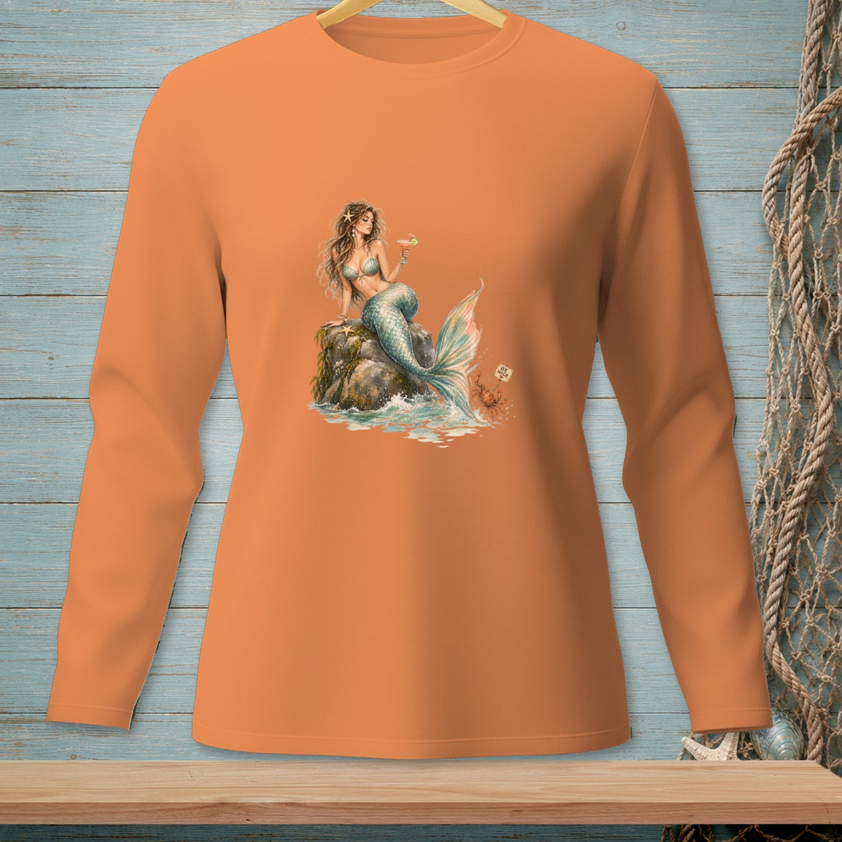 Orange long-sleeve shirt with graphic of a mermaid holding a drink on a rock.