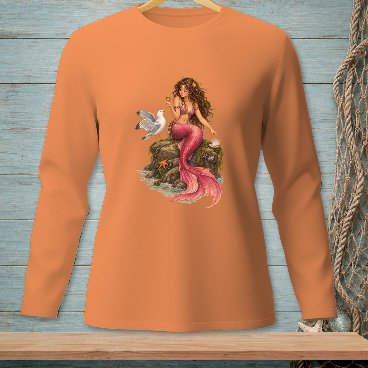 Orange long-sleeve shirt featuring a mermaid with a pink tail sitting on a rock with a seagull.