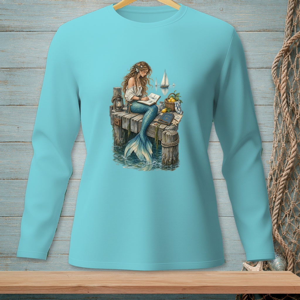 Mermaid sitting on a dock writing in a book with sailboats in the background.