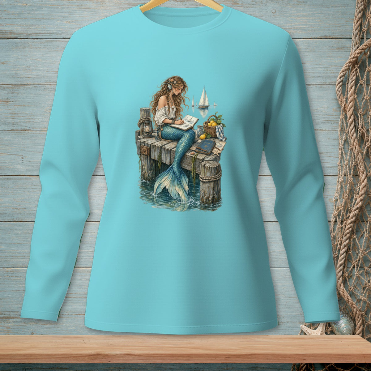 Mermaid sitting on a dock writing in a book with sailboats in the background.