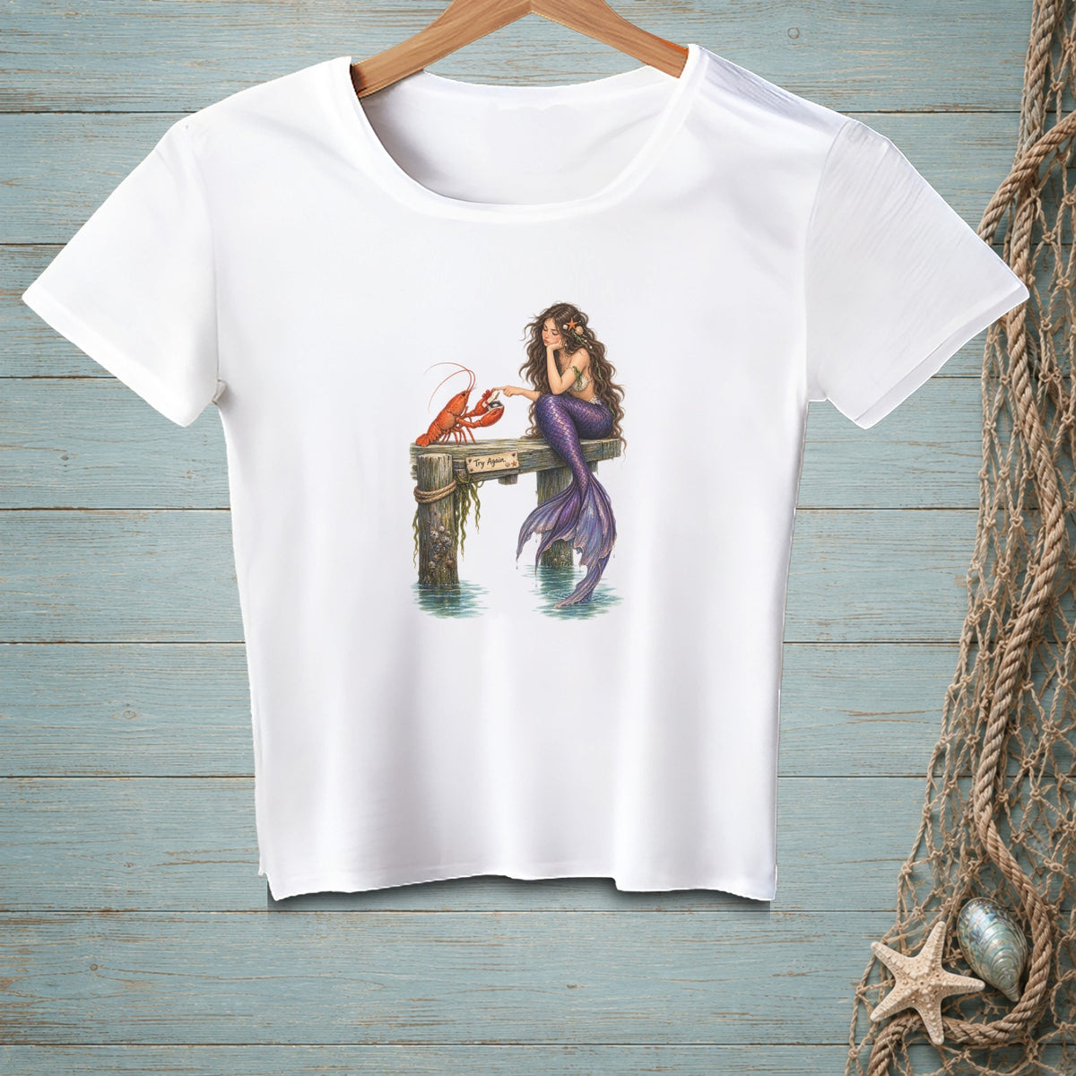 White t-shirt with a mermaid and lobster sitting on a dock.