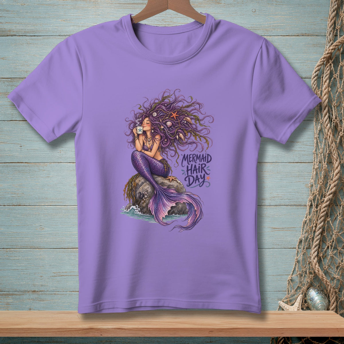 Purple t-shirt with a mermaid sitting on a rock, holding a coffee cup.