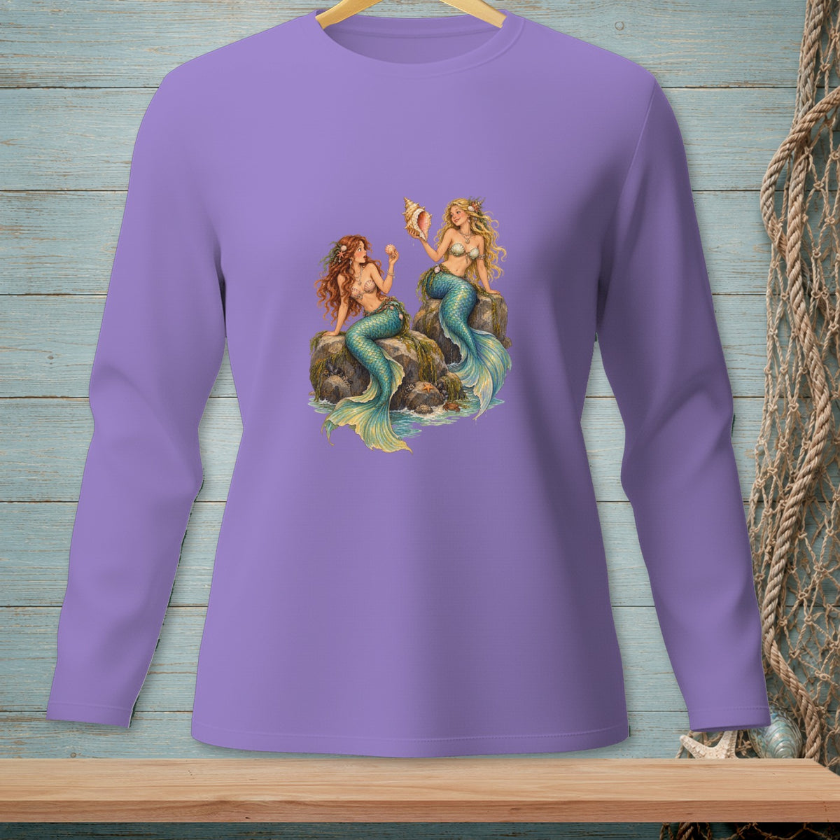 Lavender long-sleeve shirt with two mermaids sitting on rocks holding seashells.