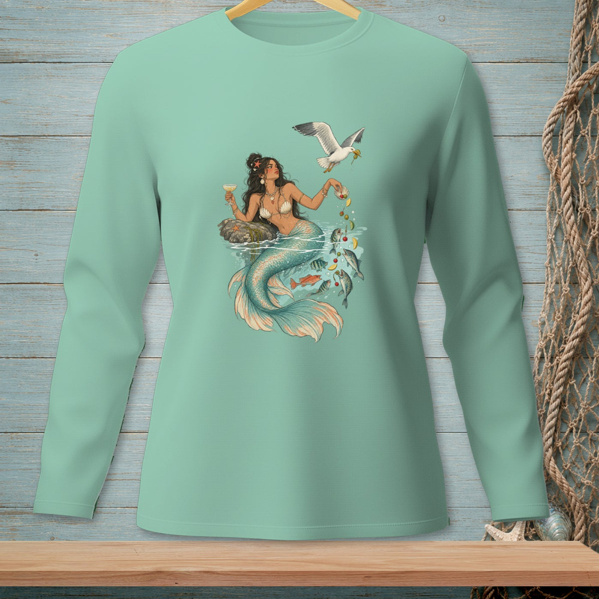 Mint long-sleeve t-shirt with a graphic of a mermaid holding a drink and a seagull overhead.
