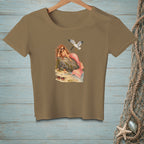 T-shirt with a mermaid resting on a rock near the water with a seagull overhead.