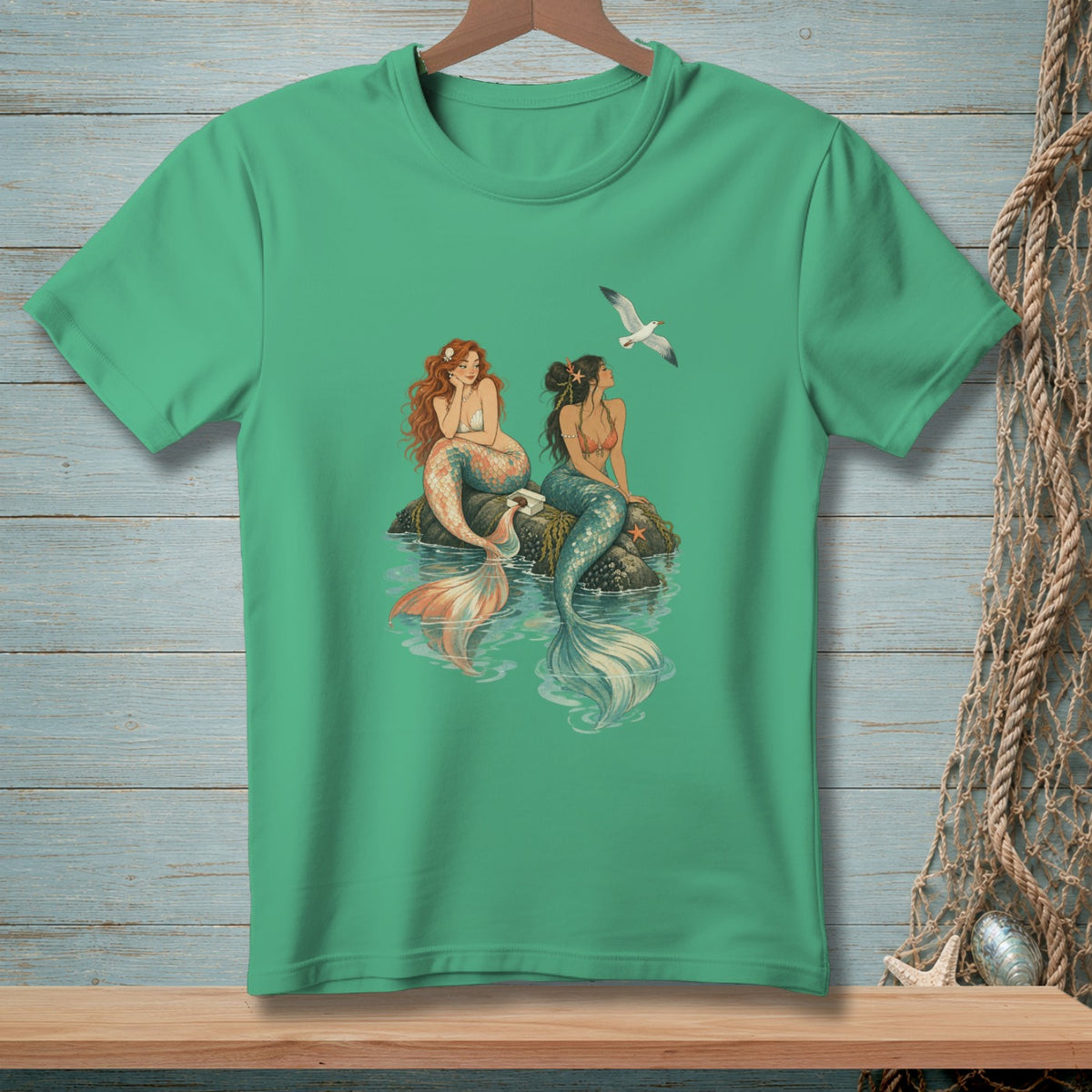 Two mermaids sit on a rock while a seagull flies overhead.