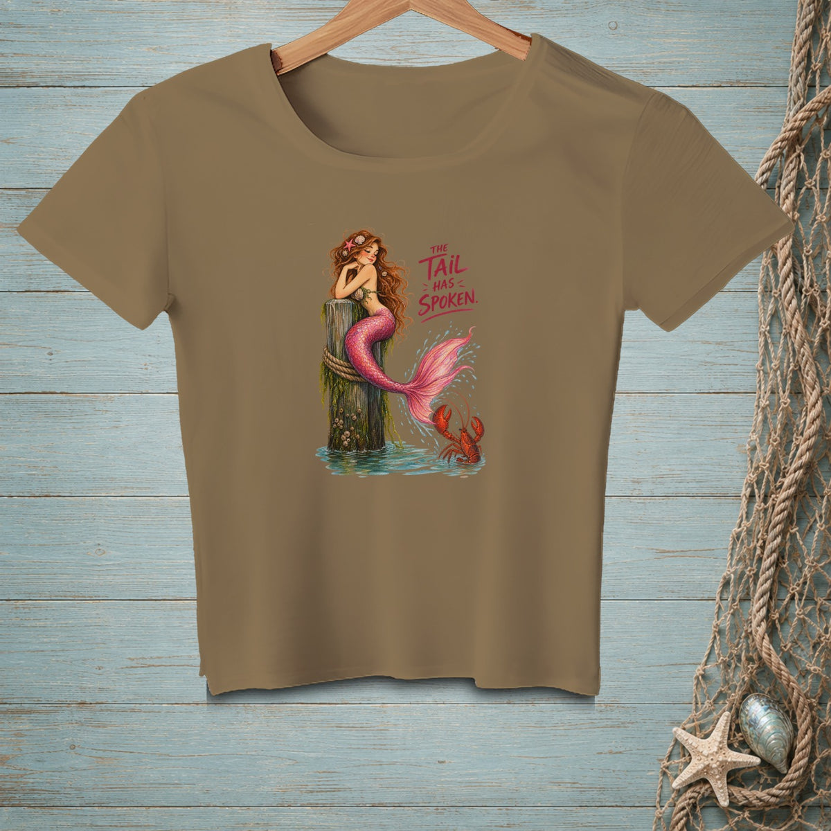 Brown t-shirt featuring a mermaid on a wooden post with text "THE TAIL HAS SPOKEN."