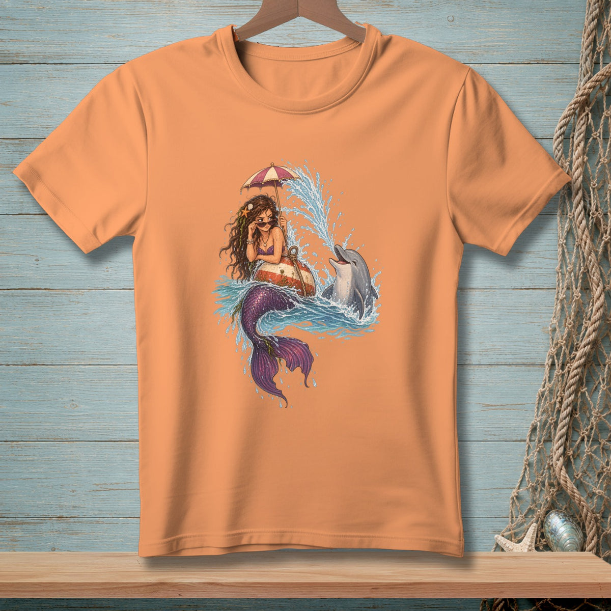 Mermaid and dolphin with umbrella in ocean waves graphic on an orange t-shirt.