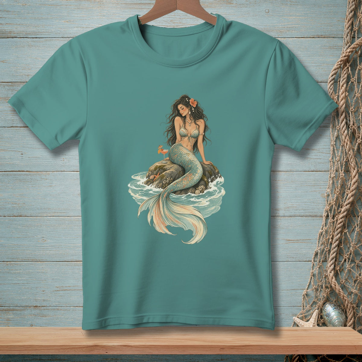 Teal t-shirt with vintage mermaid illustration on a rock in the ocean.