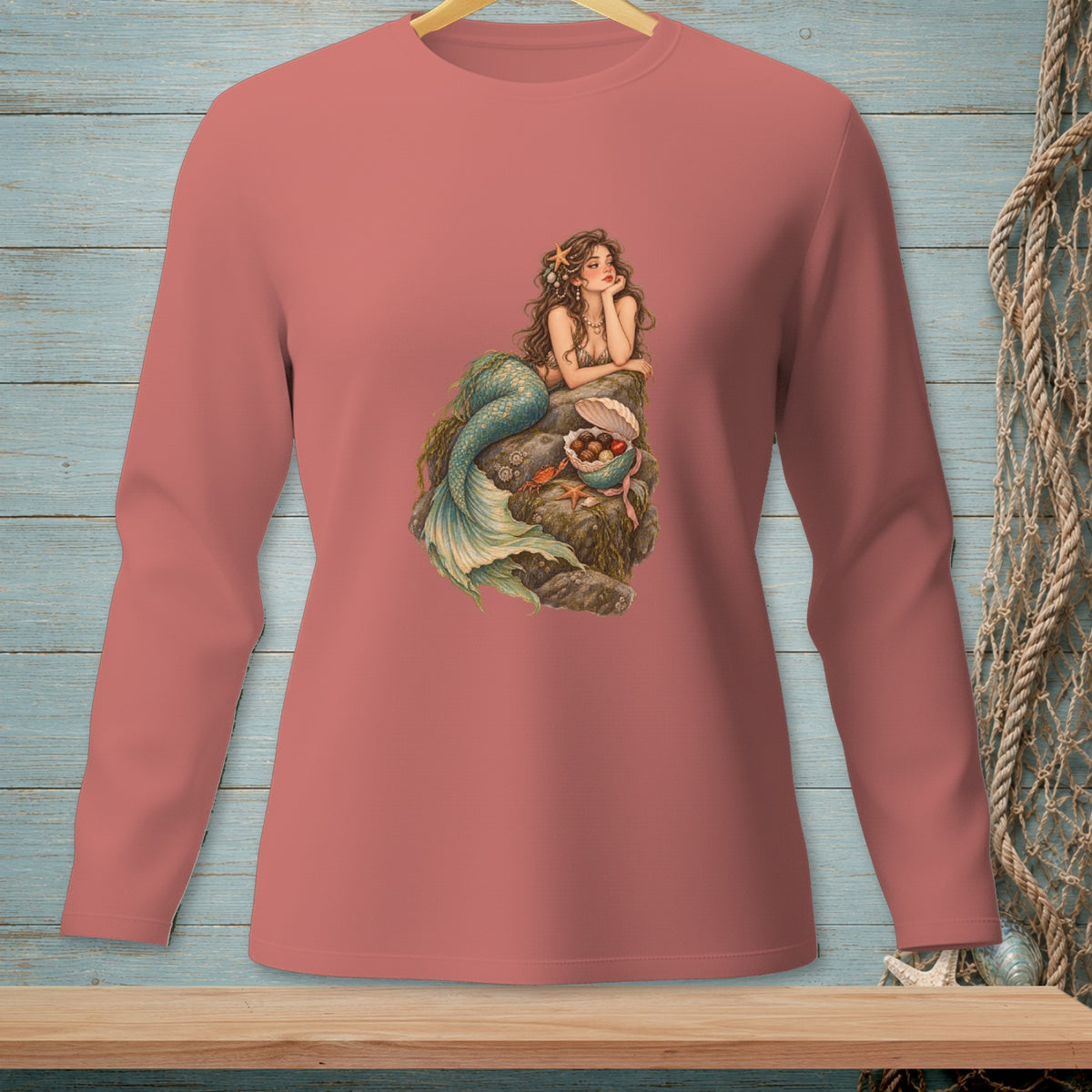 Long-sleeve salmon shirt with a mermaid graphic sitting on a rock.