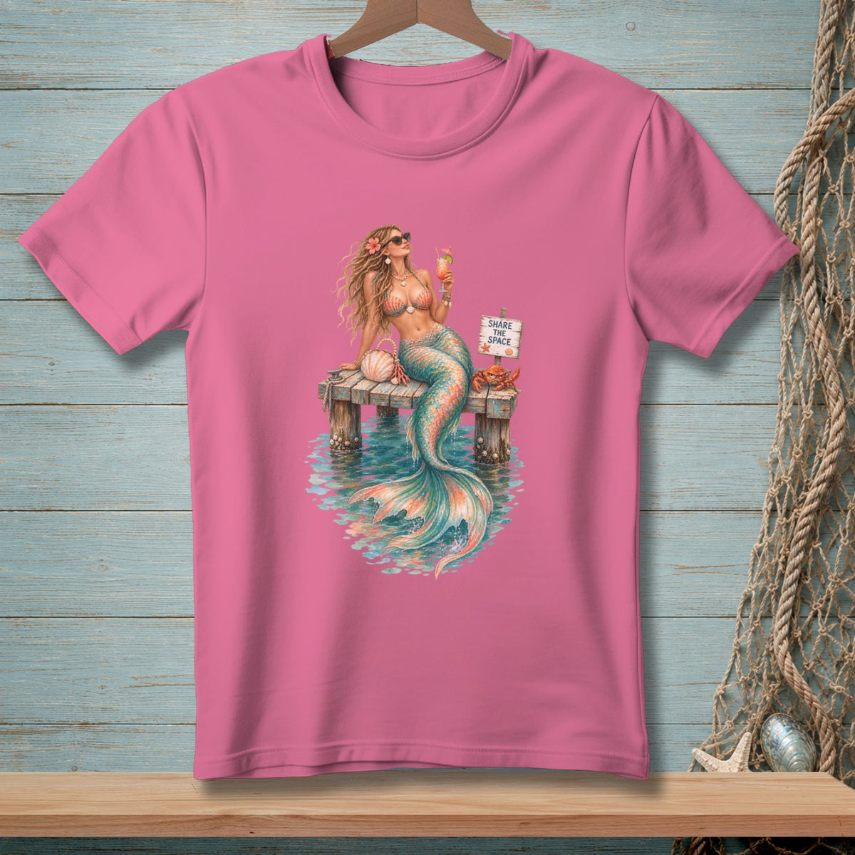 Pink t-shirt with a mermaid on a dock holding a drink and a sign that says "Share The Space."