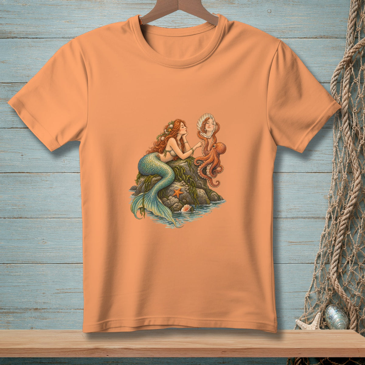 Peach t-shirt with a mermaid and octopus on a rock with shells and starfish.