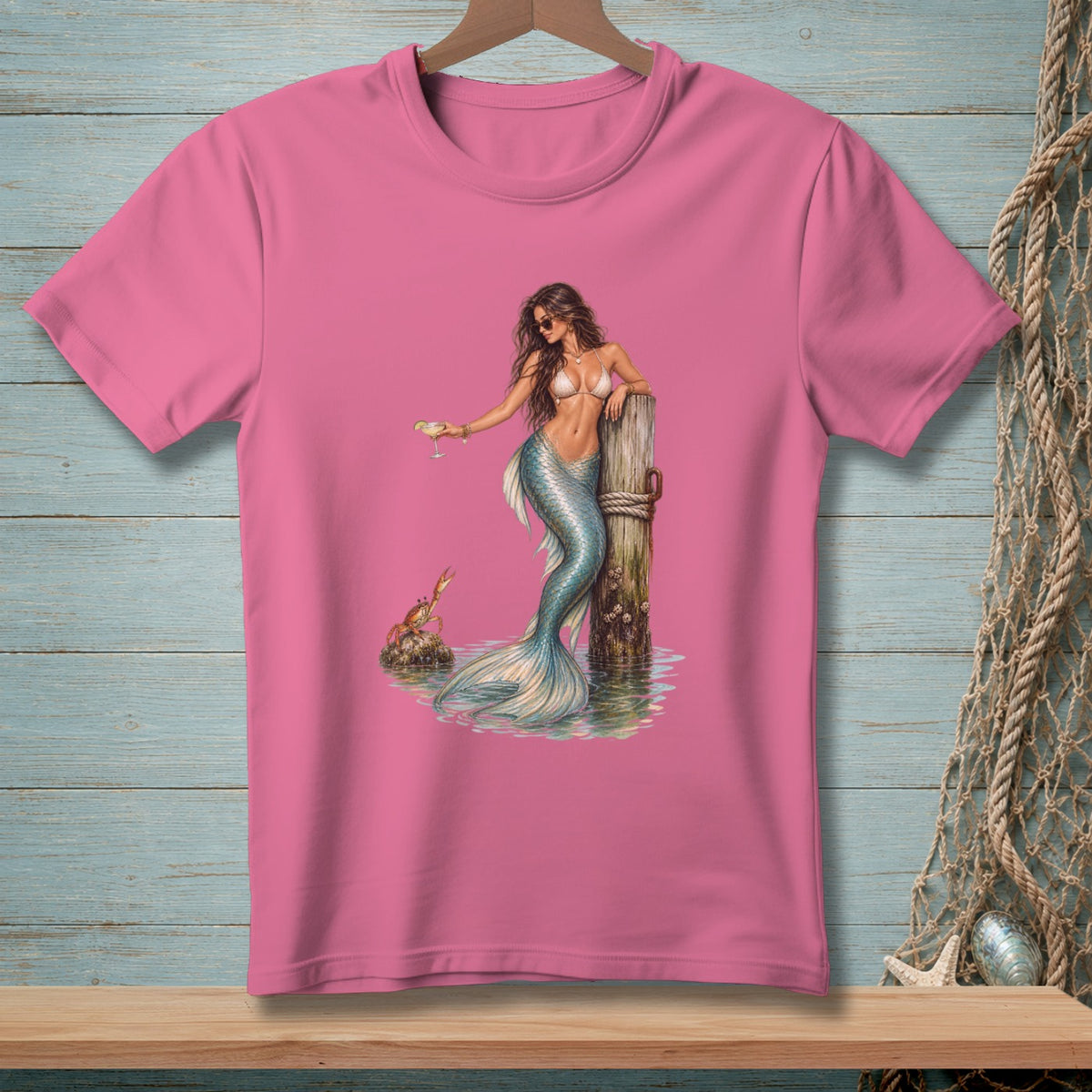 Pink t-shirt with a mermaid holding a drink by a dock with a crab.
