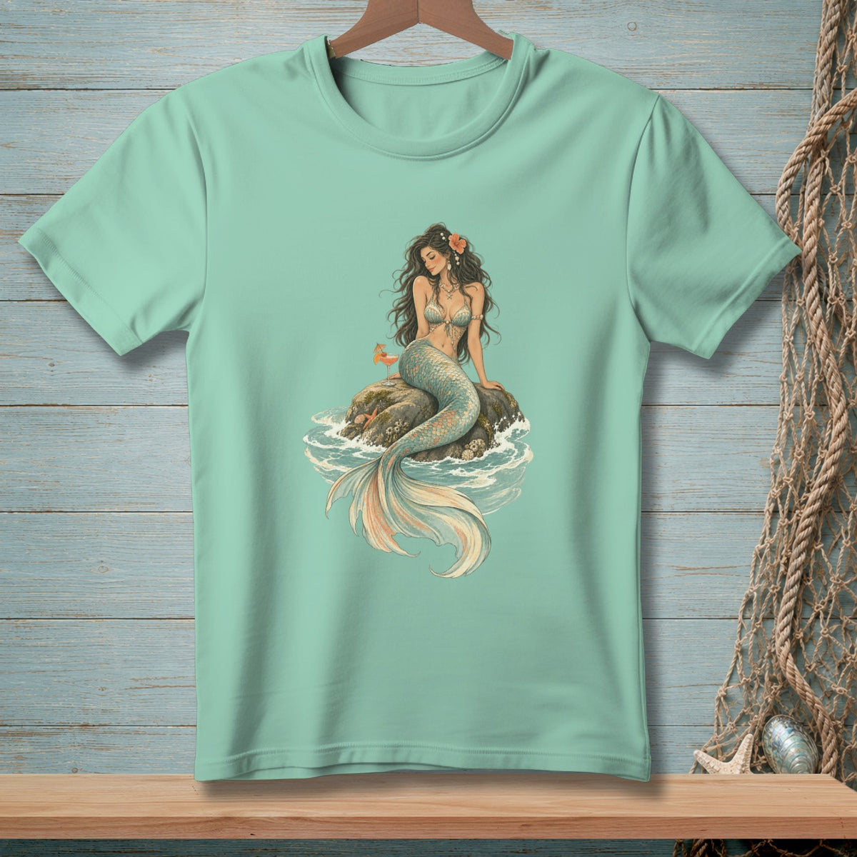 Mint green t-shirt with a mermaid sitting on a rock in the ocean.