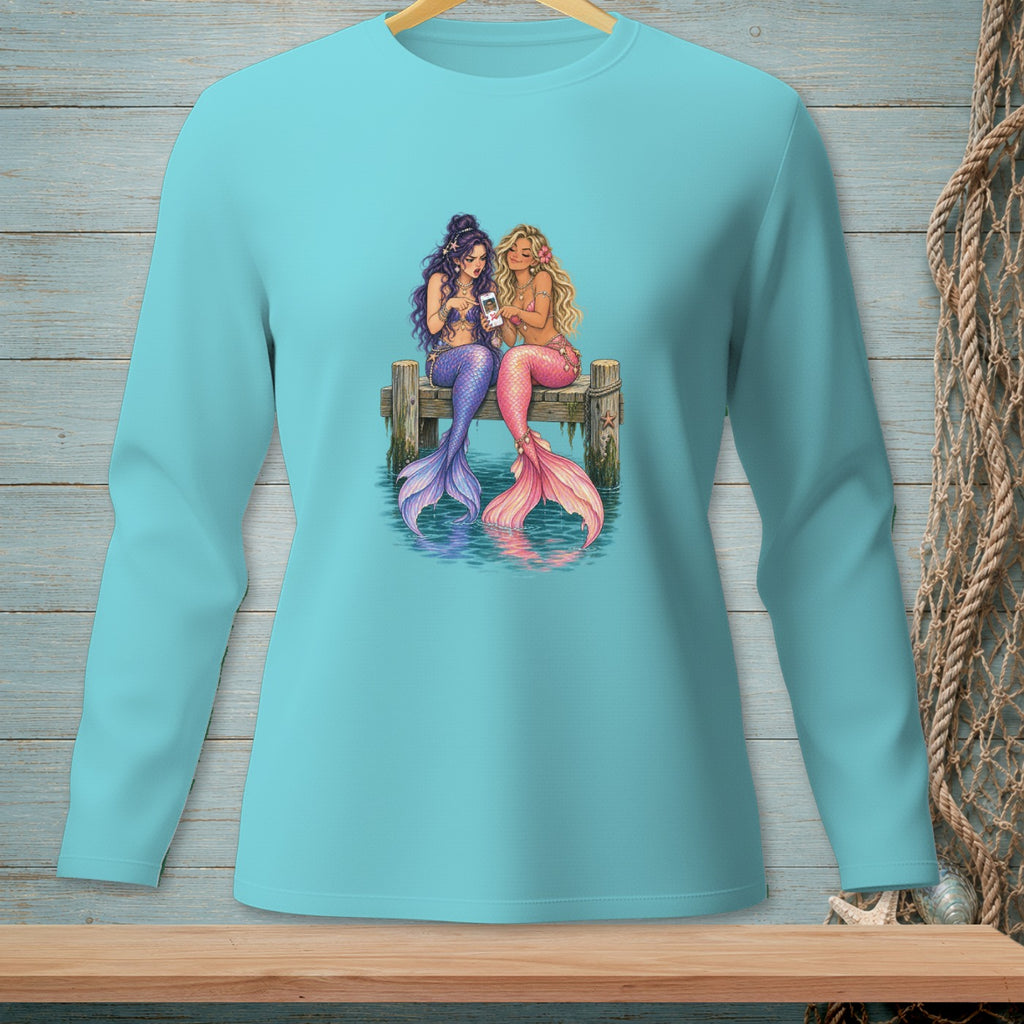 Two mermaids with colorful tails sit on a dock looking at a smartphone.