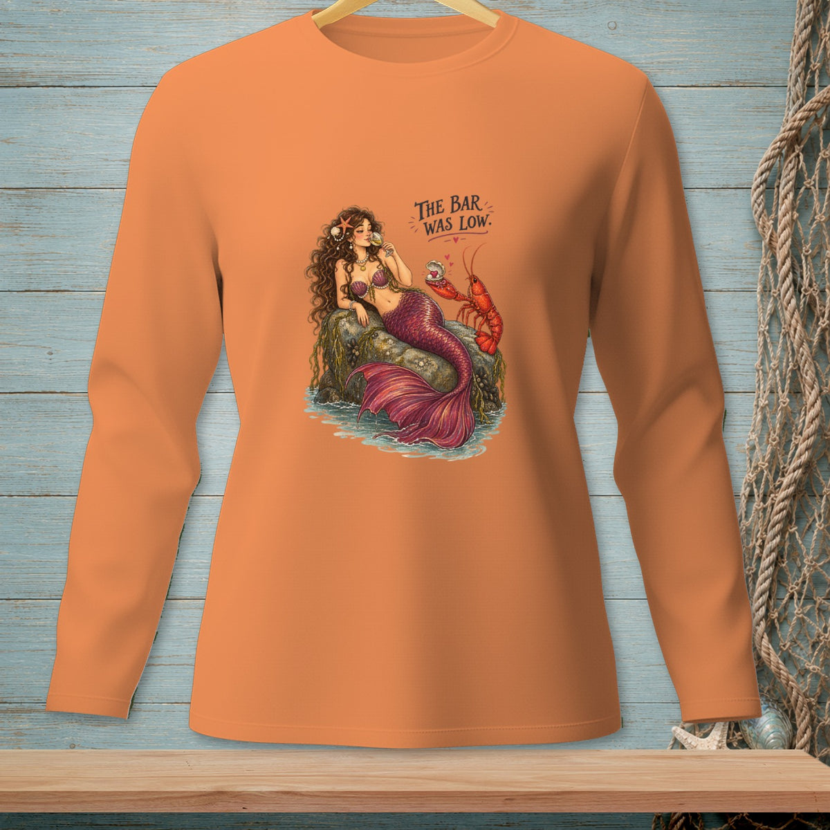 Mermaid and lobster design with text "The bar was low" on an orange long-sleeve shirt.