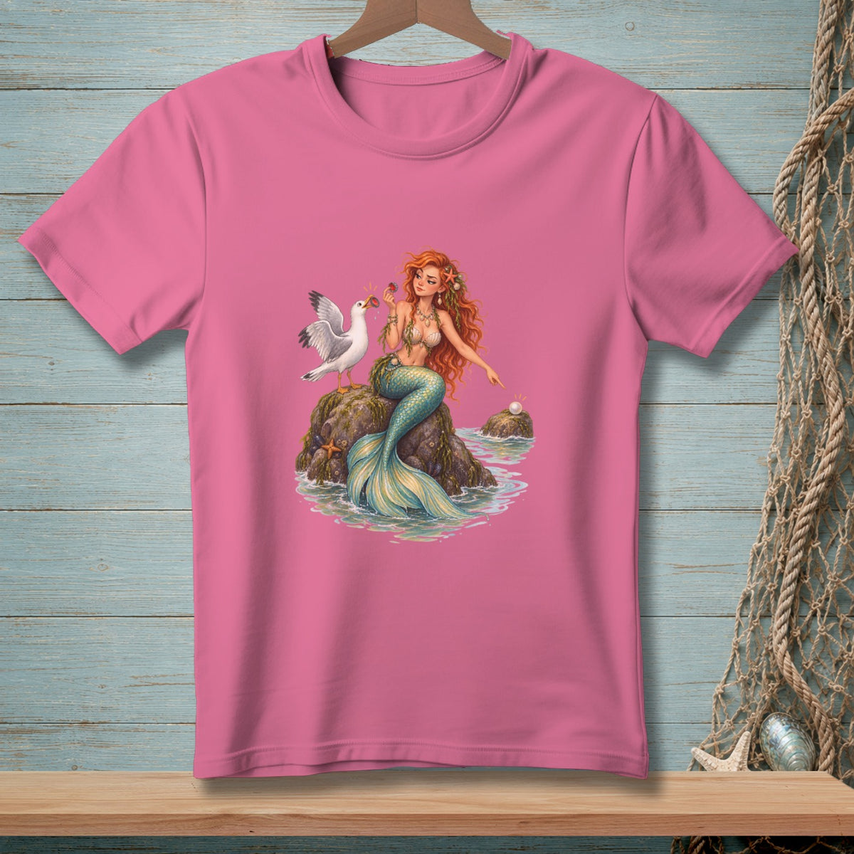 Pink t-shirt with illustration of a mermaid and a seagull on a rock.