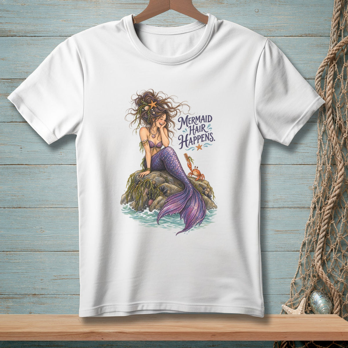 White t-shirt with a mermaid sitting on a rock, with text "Mermaid Hair Happens."