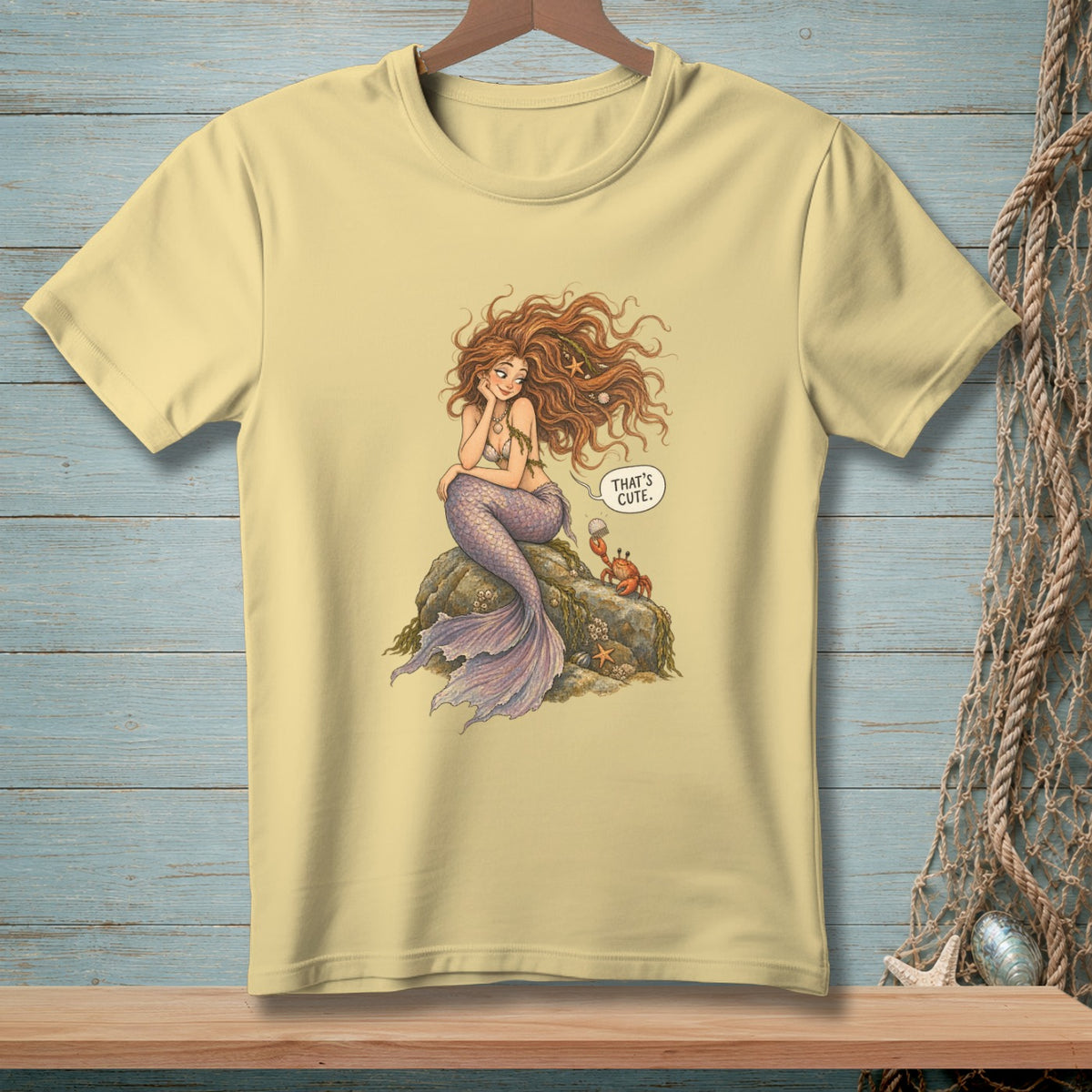 Light yellow t-shirt with a mermaid, crab, and text bubble saying "That's cute."