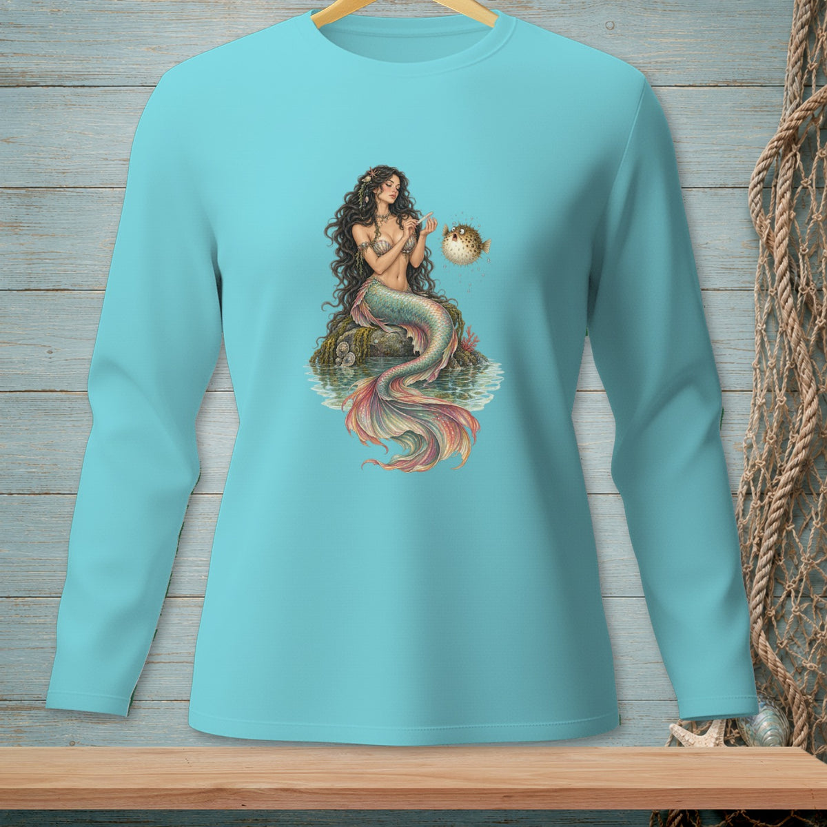 Mermaid sitting on rock with pufferfish on turquoise long sleeve shirt.