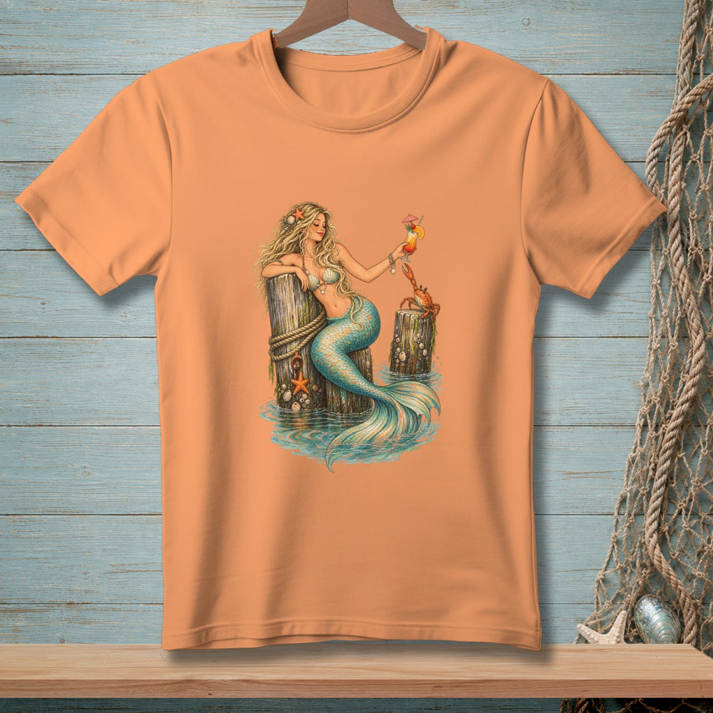 Peach t-shirt featuring a mermaid with a cocktail and a crab by a wooden post.