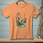 Peach t-shirt featuring a mermaid with a cocktail and a crab by a wooden post.