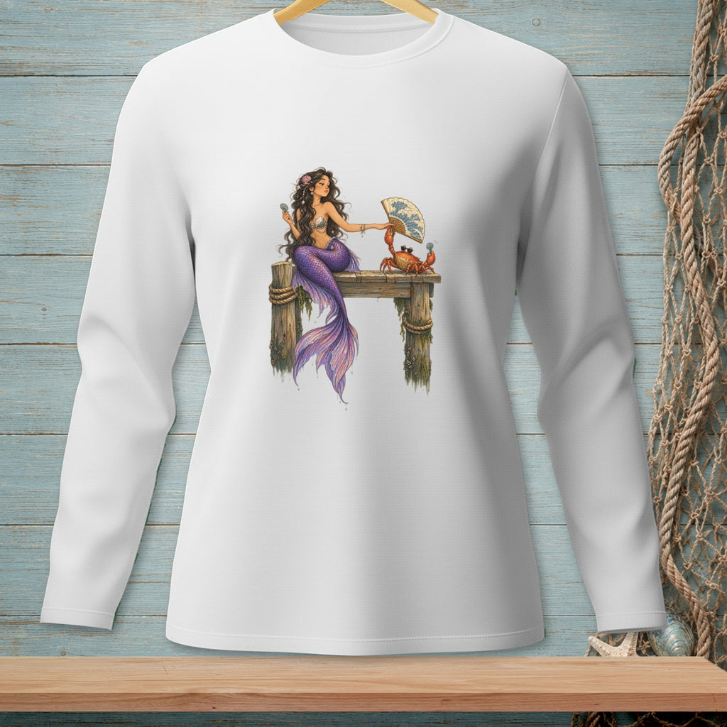 White long-sleeve shirt with a mermaid and crab illustration sitting on a wooden dock.