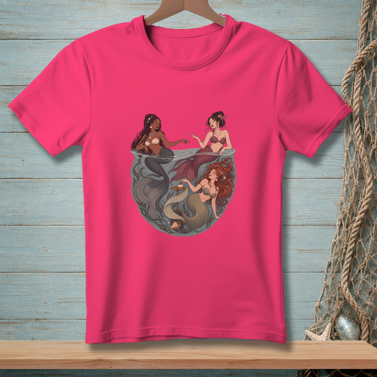 Three mermaids gathered in a circular design on a bright pink t-shirt.
