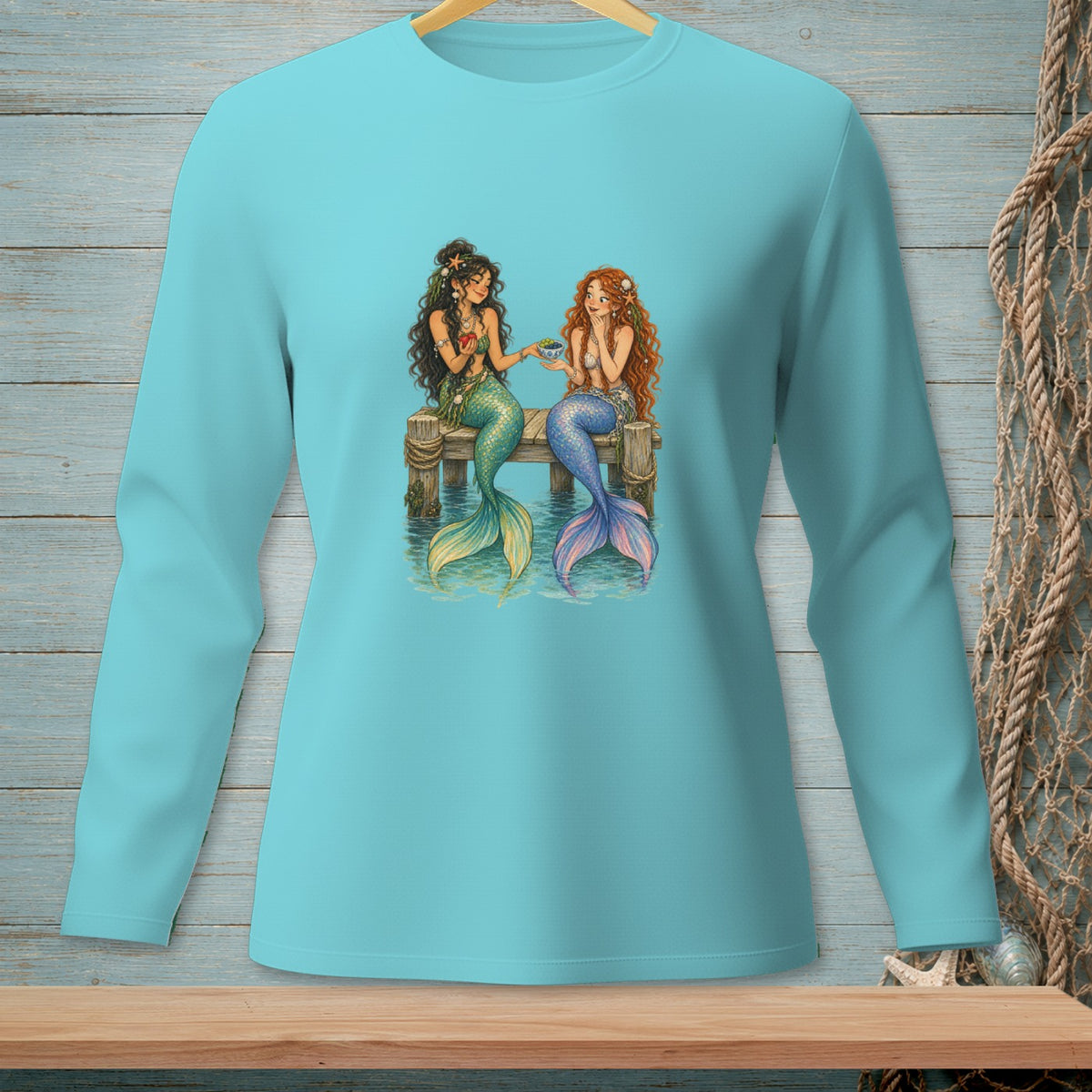 Two mermaids with tails sit on a wooden pier, one offering a fruit to the other.