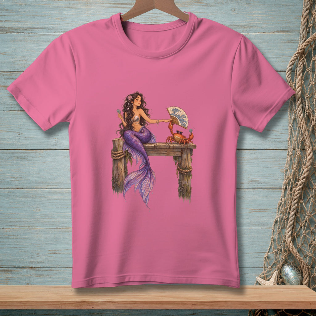 Pink t-shirt with a mermaid and crab sitting on a wooden pier, holding a fan.