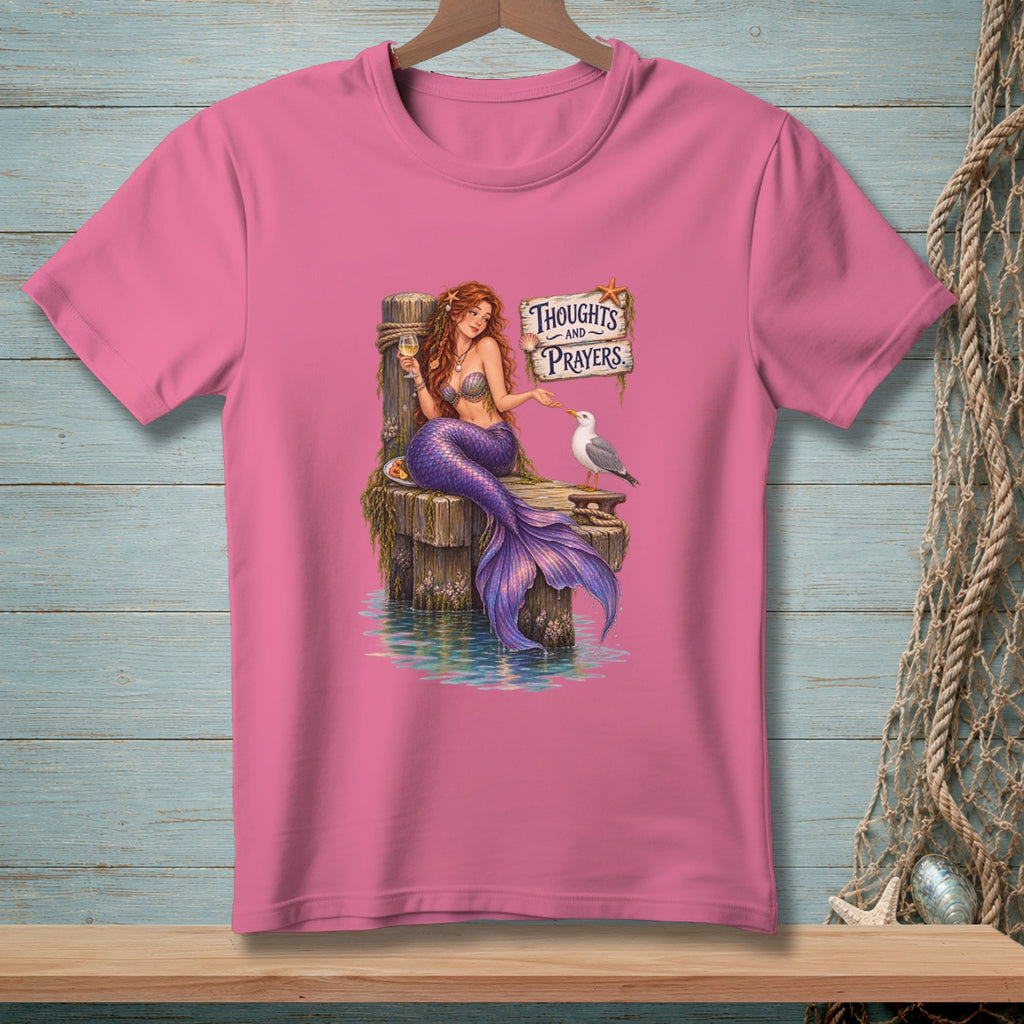 Pink t-shirt with a mermaid sitting on a dock, feeding a seagull, with "Thoughts and Prayers" sign.