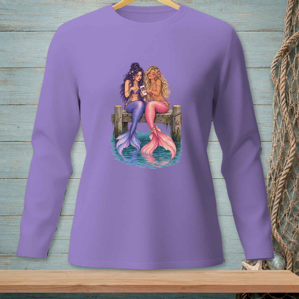 Two mermaids with colorful tails sit on a dock, looking at a phone.